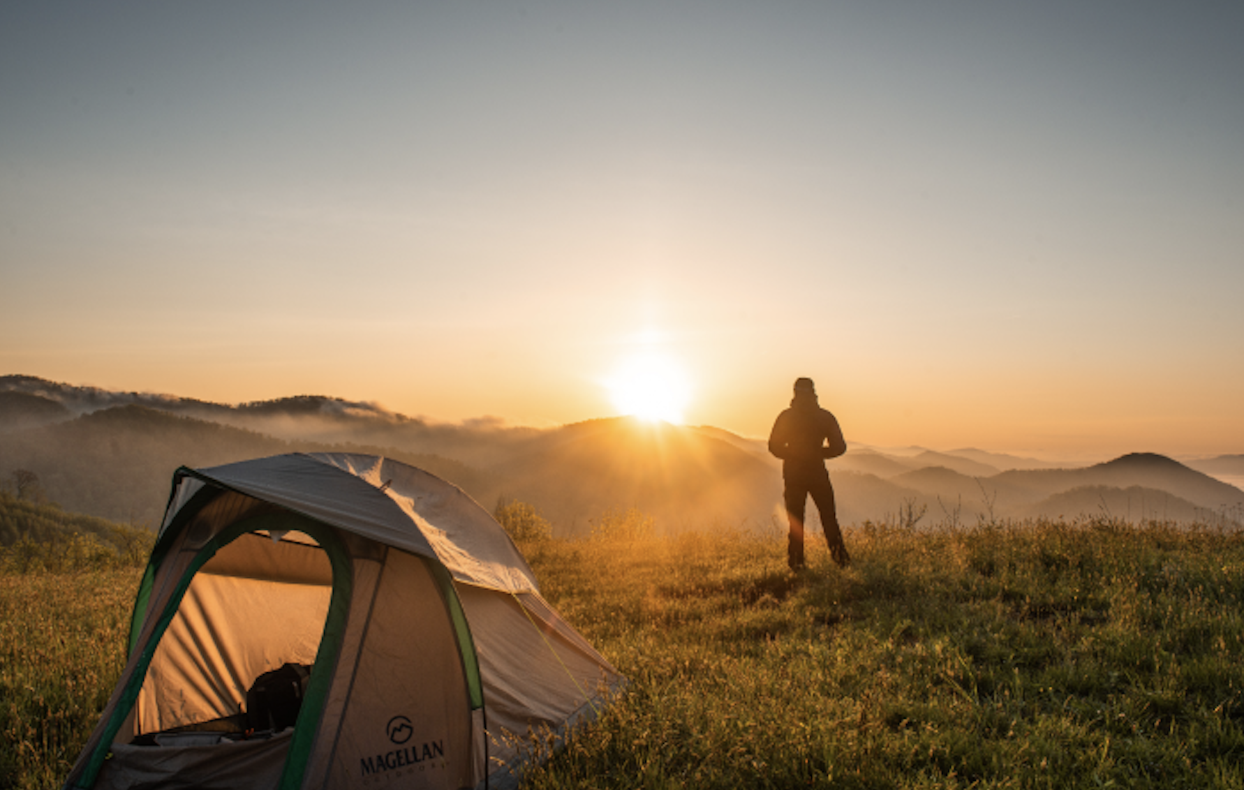 A person watching the sunrise by a tent